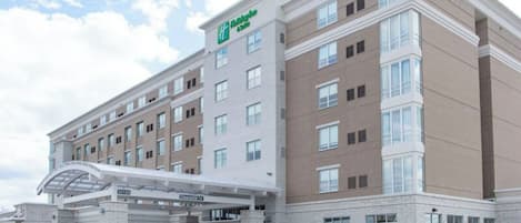 A multi-story hotel with a prominent green logo, a covered entrance, and a brick facade.
