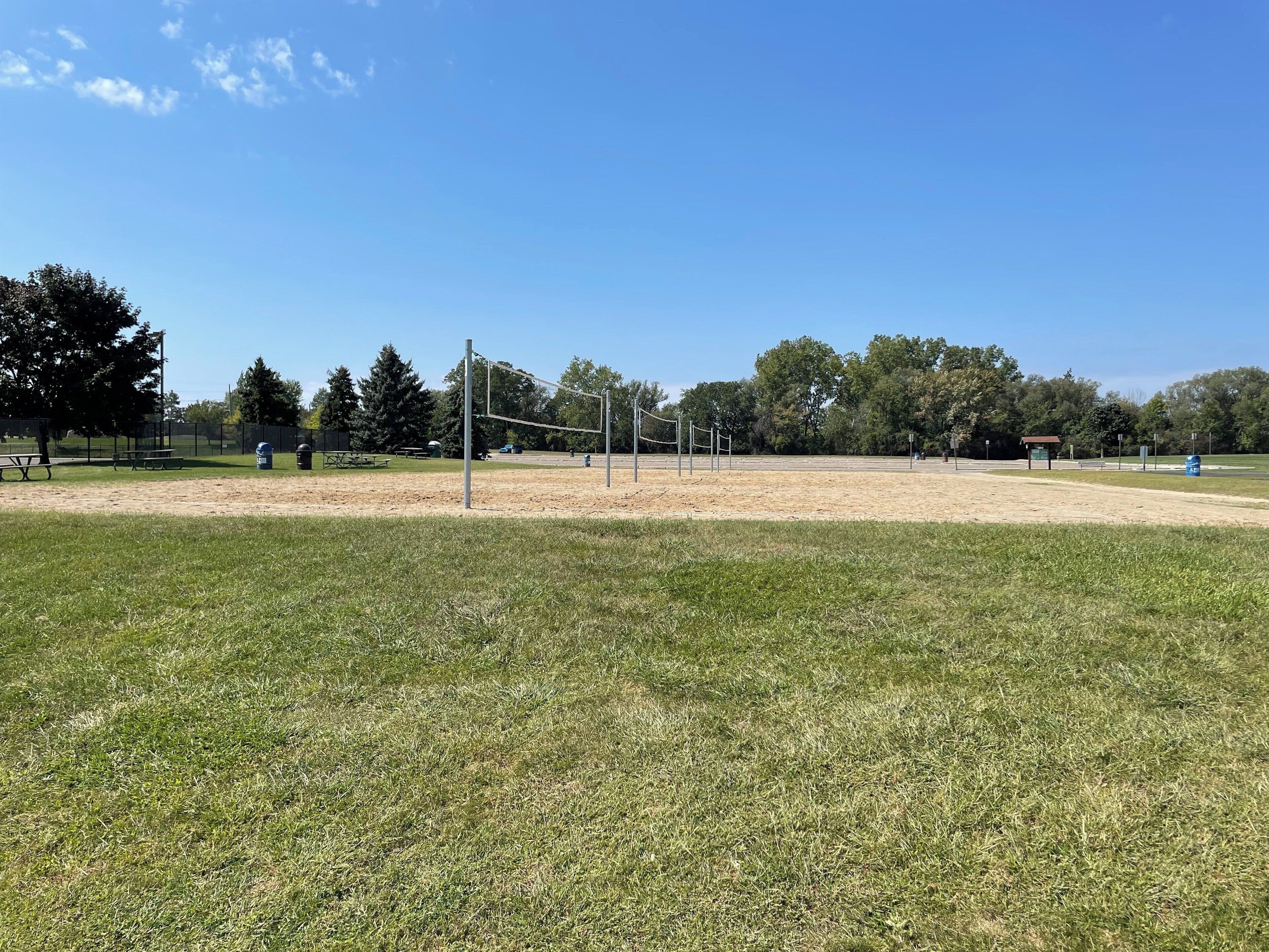 A park with a volleyball net, picnic tables, and a shelter.