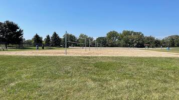 A park with a volleyball net, picnic tables, and a shelter.