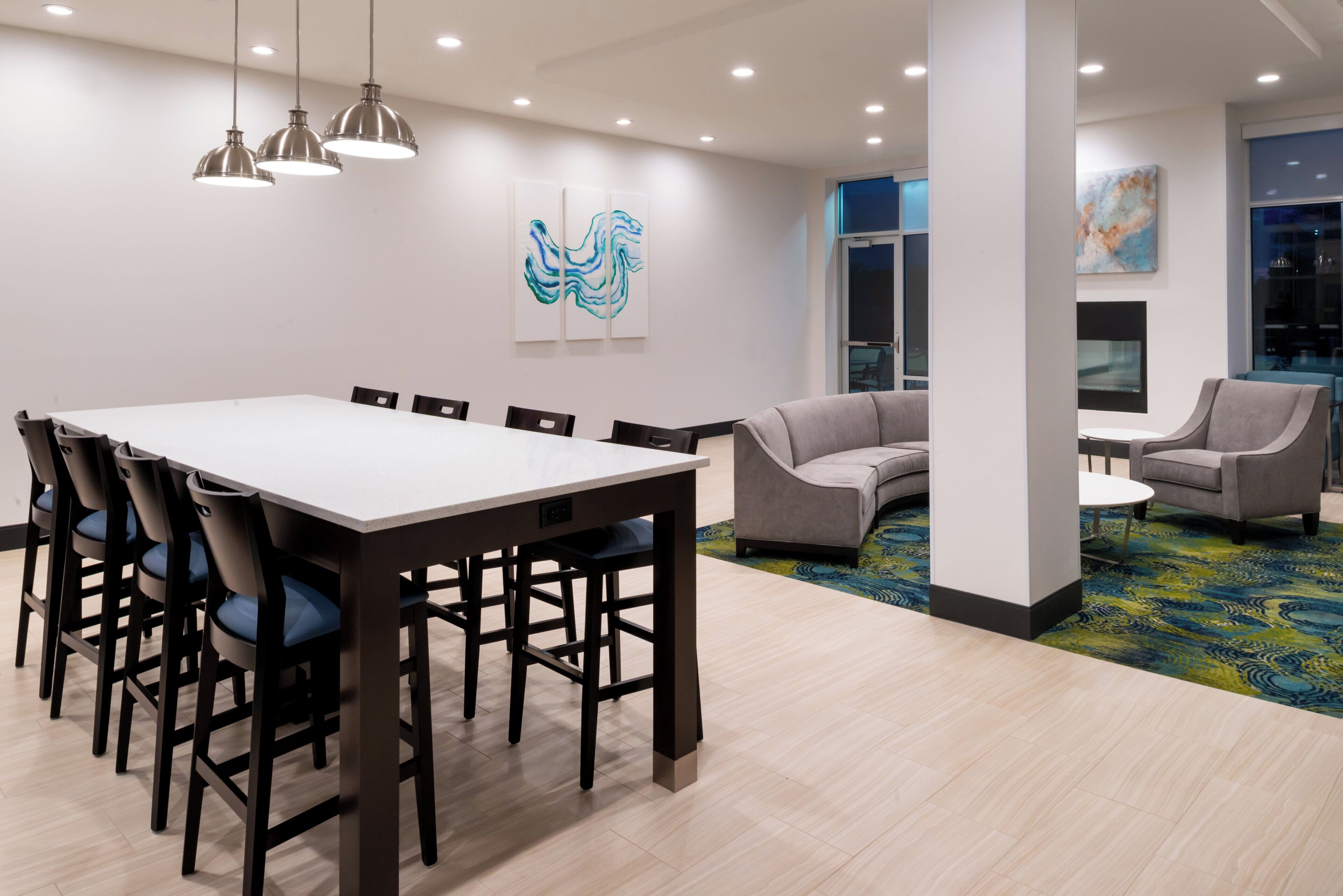 A conference room with a large table and chairs, a sofa, and a coffee table. There are wall-mounted art pieces and a window with a view.