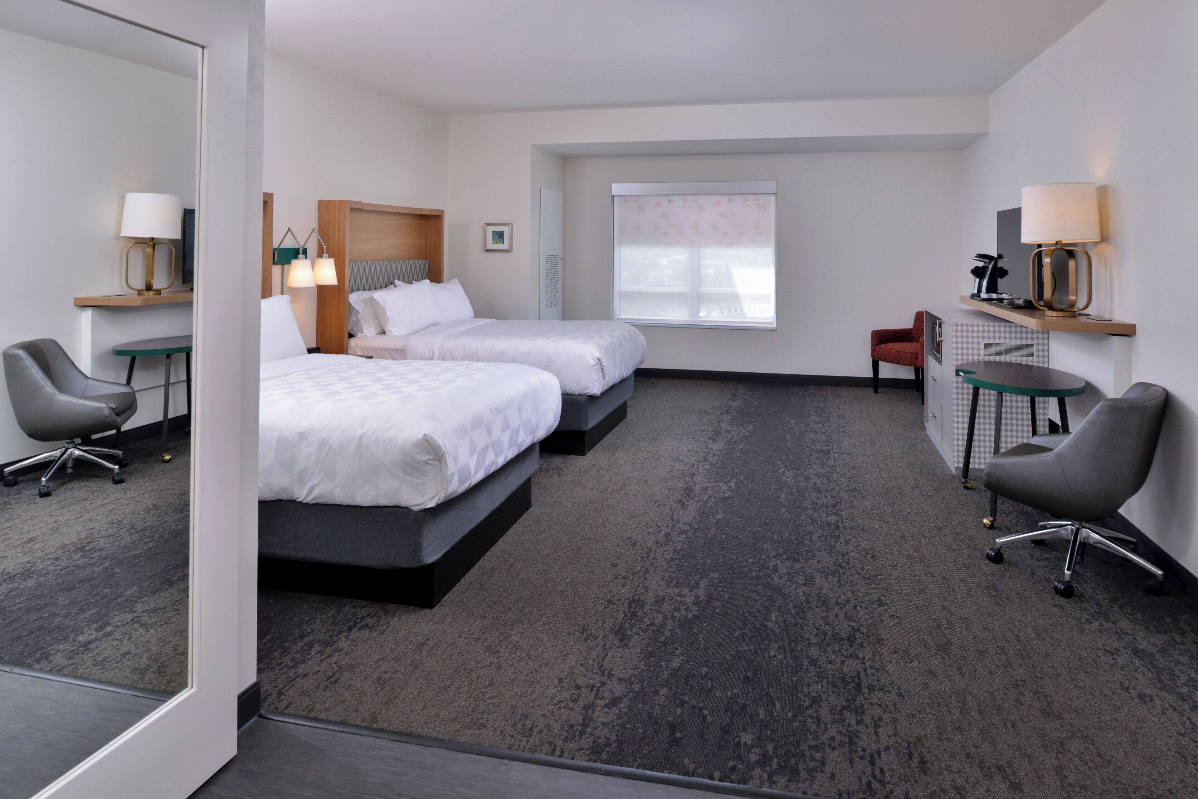 A hotel room with two beds, a desk, a chair, a small table, and a window.