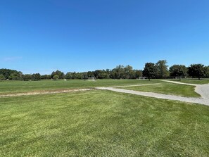 A large, open grassy field with multiple soccer goals and a paved path.
