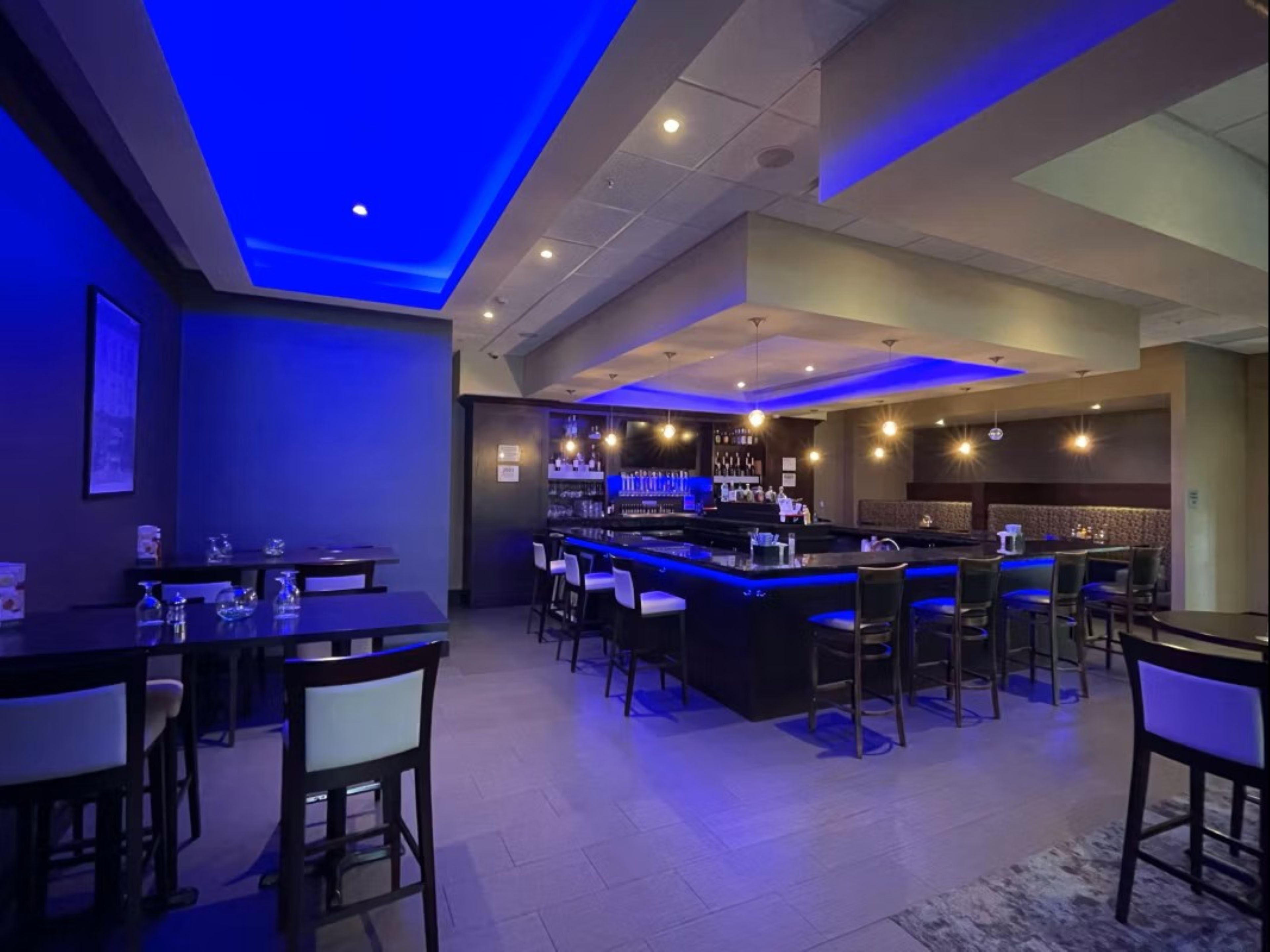 Zona de bar con barra, taburetes y área de estar con mesas y sillas.