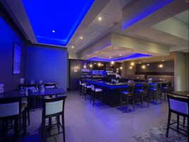 Zona de bar con barra, taburetes y área de estar con mesas y sillas.