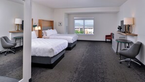 A hotel room with two beds, a desk, a chair, and a window with a view.