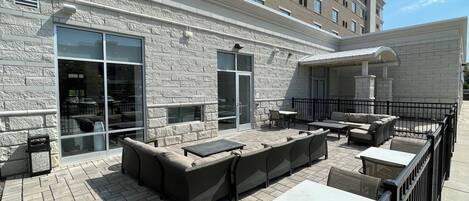 An outdoor patio area with seating arrangements, including sofas and tables, and a covered section with a fireplace.