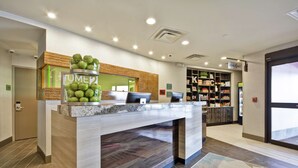 A reception area with a counter, a display of green apples, and a sign that reads "HOME2". - Home2 Suites by Hilton KCI Airport (Kansas City)