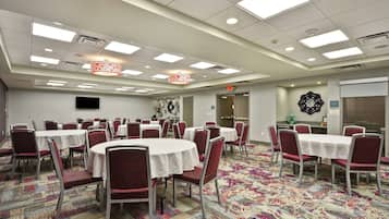 A conference room with round tables and red chairs, carpeted floor, and ceiling lights.