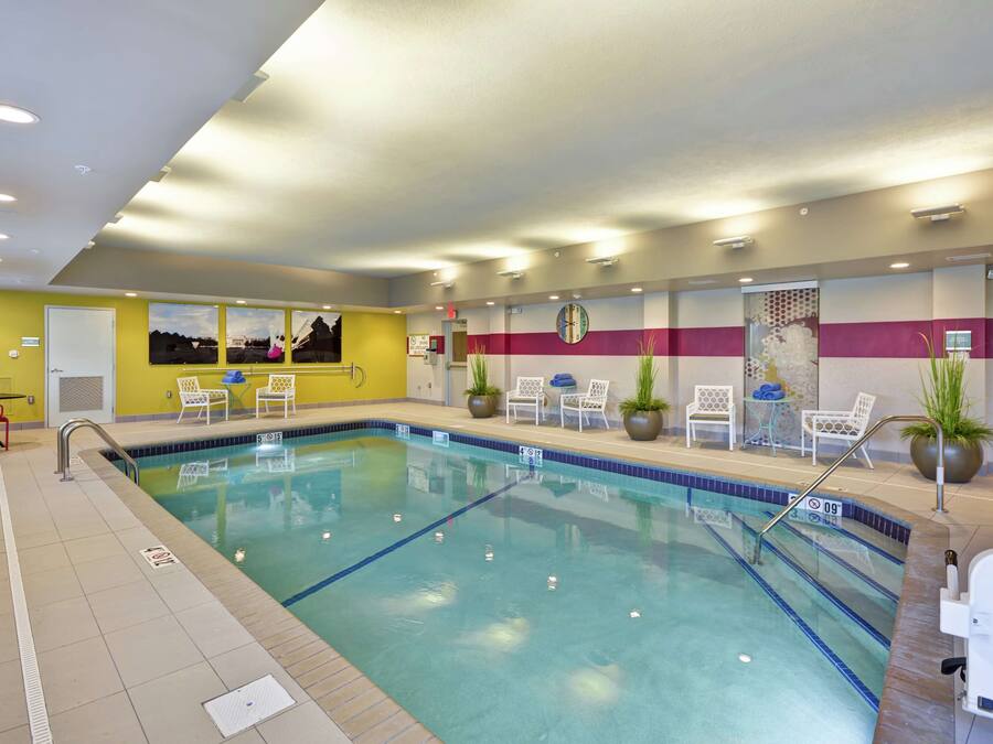 A swimming pool with a tiled deck, lounge chairs, and a clock on the wall.