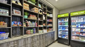 A grocery store with shelves stocked with snacks, beverages, and packaged goods. There are two refrigerated display cases labeled "cold" and "really cold." - Home2 Suites by Hilton KCI Airport (Kansas City)
