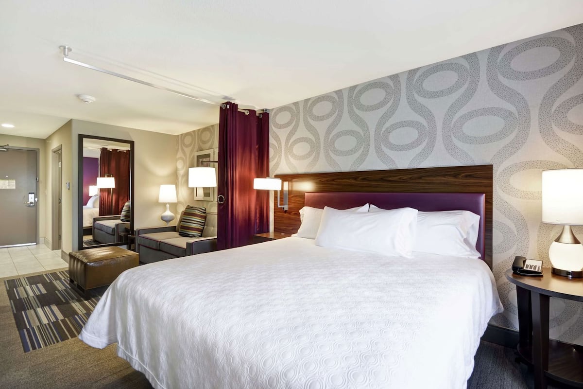 Une chambre d’hôtel avec un grand lit, une table de chevet, un bureau, une chaise, un miroir et une porte.