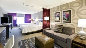 A hotel room with a bed, a sofa, a desk with a TV, and a lamp. - Home2 Suites by Hilton KCI Airport (Kansas City)