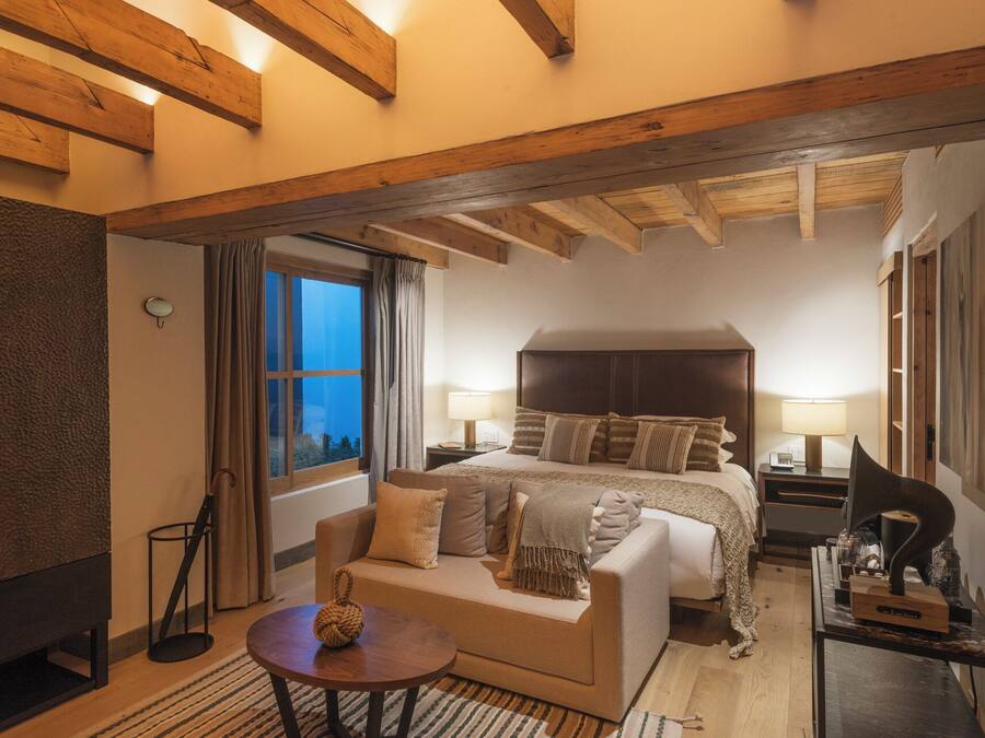 Una habitación de hotel con cama, sofá, una mesita, lámpara y ventana con cortinas.