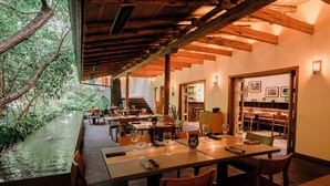 A restaurant with a long dining table, chairs, and a view of a water feature and greenery. - La Casa Rodavento - Adults Only (Valle de Bravo)