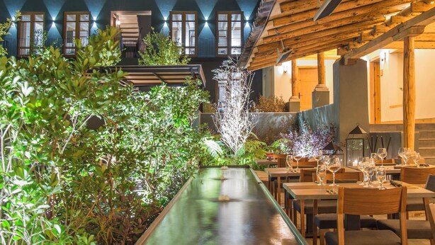 A restaurant with a long water feature, wooden tables, and chairs, surrounded by greenery and trees. - La Casa Rodavento - Adults Only (Valle de Bravo)