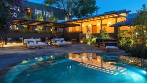 A modern outdoor pool area with lounge chairs and a pergola, surrounded by lush greenery and a well-lit building. - La Casa Rodavento - Adults Only (Valle de Bravo)