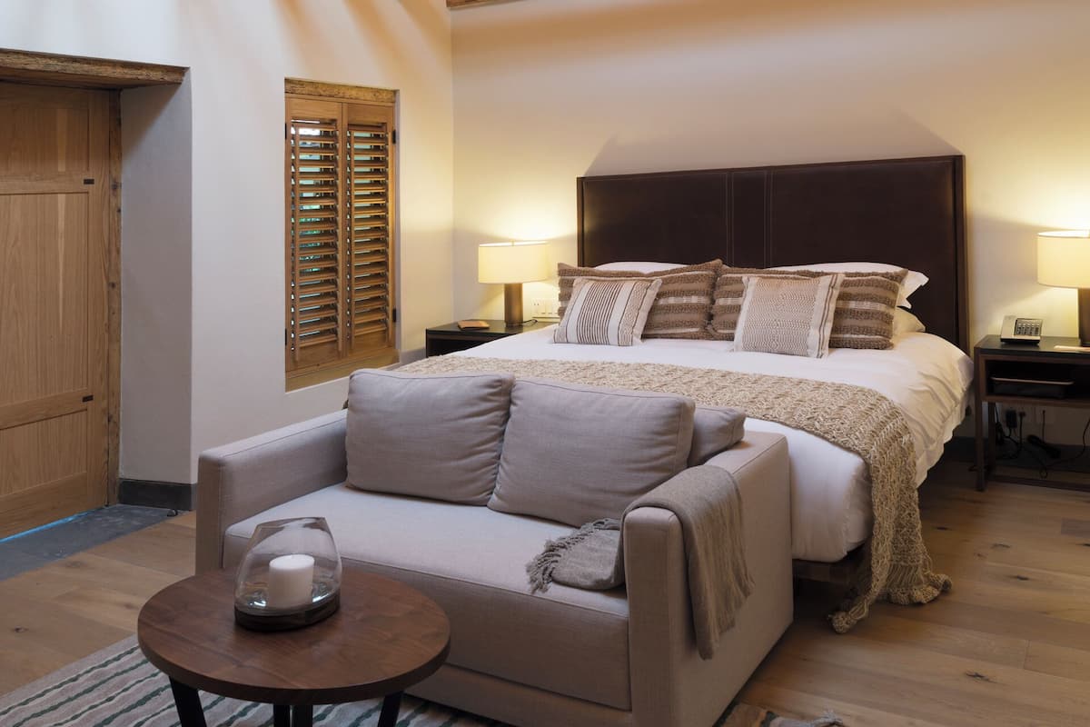Ein Schlafzimmer mit Holzboden, einem Bett mit Kopfteil, einem Nachttisch, einem Sofa und einem kleinen Tisch mit Kerze.