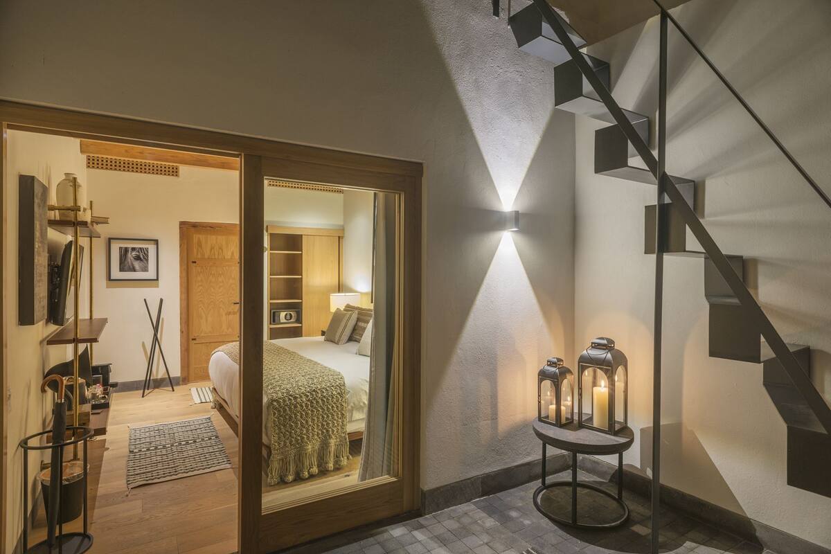 Ein Hotelzimmer mit einem Bett, einem Spiegel, einer Holztür, einer Treppe und einer Wandleuchte.