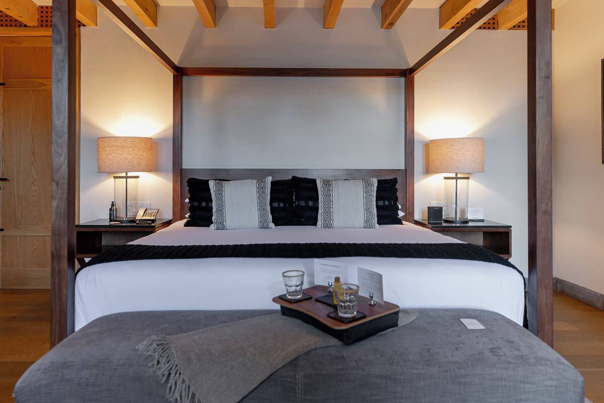 Ein Himmelbett mit einer grau gepolsterten Bank, Holzbalken und einem Streifen Teppich.