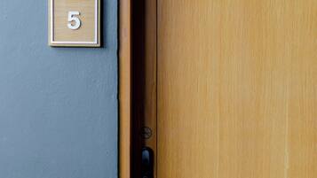 A wooden door with a metal handle and a small wooden plaque with the number 5 on a grey wall.