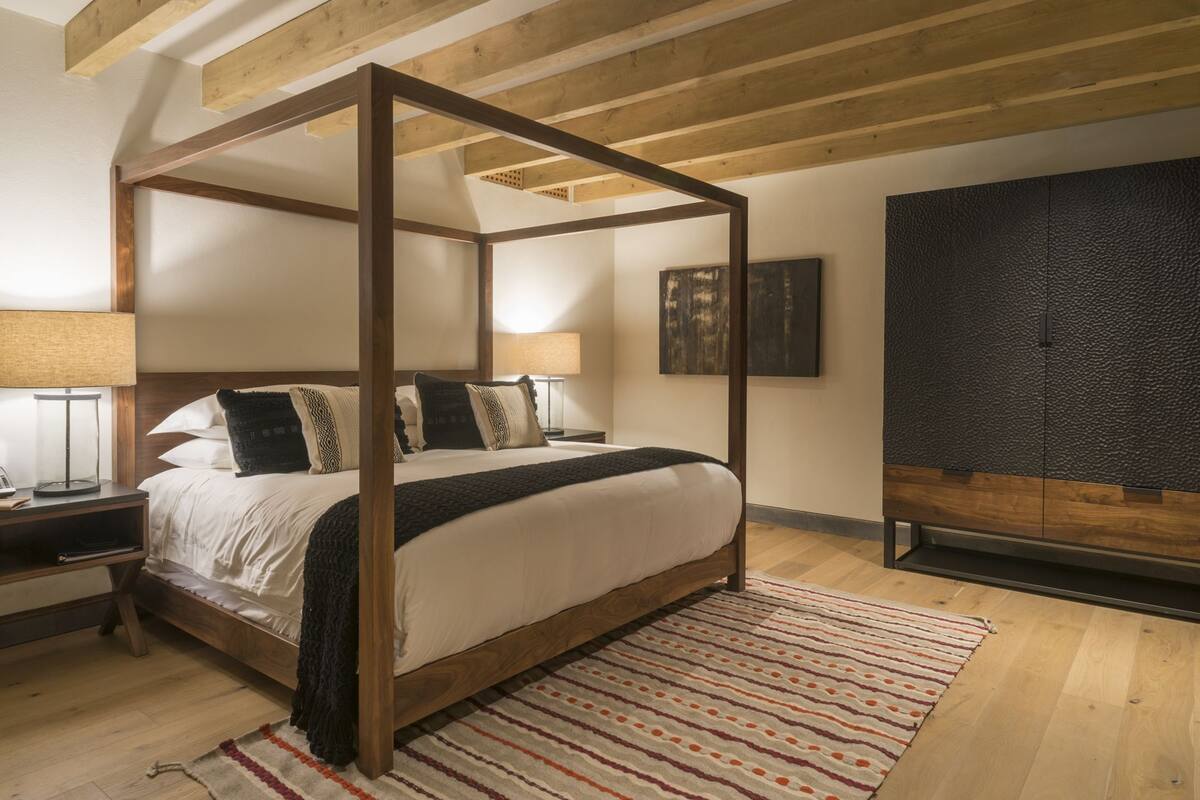 Ein Himmelbett mit Holzgestell, ein großes abstraktes Gemälde und eine strukturierte schwarze Kommode.