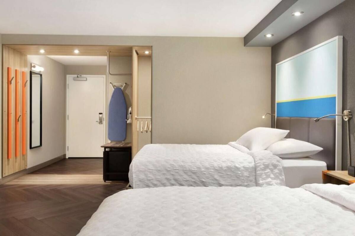 A hotel room with two beds, a mirror, a wardrobe, and a painting on the wall.