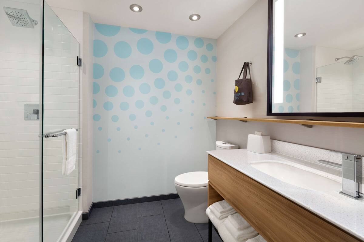 A modern bathroom with a glass shower enclosure, a toilet, a sink with a wooden vanity, and a mirror.