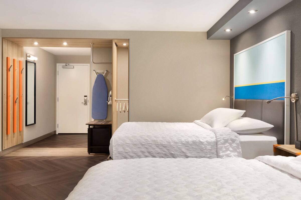 A hotel room with two beds, a large mirror, a wardrobe, and a view of the hallway.
