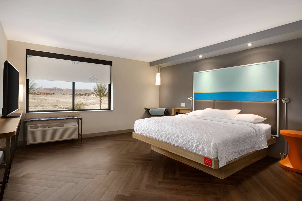 A modern bedroom with a bed, a TV, a heater, and a view of the desert.