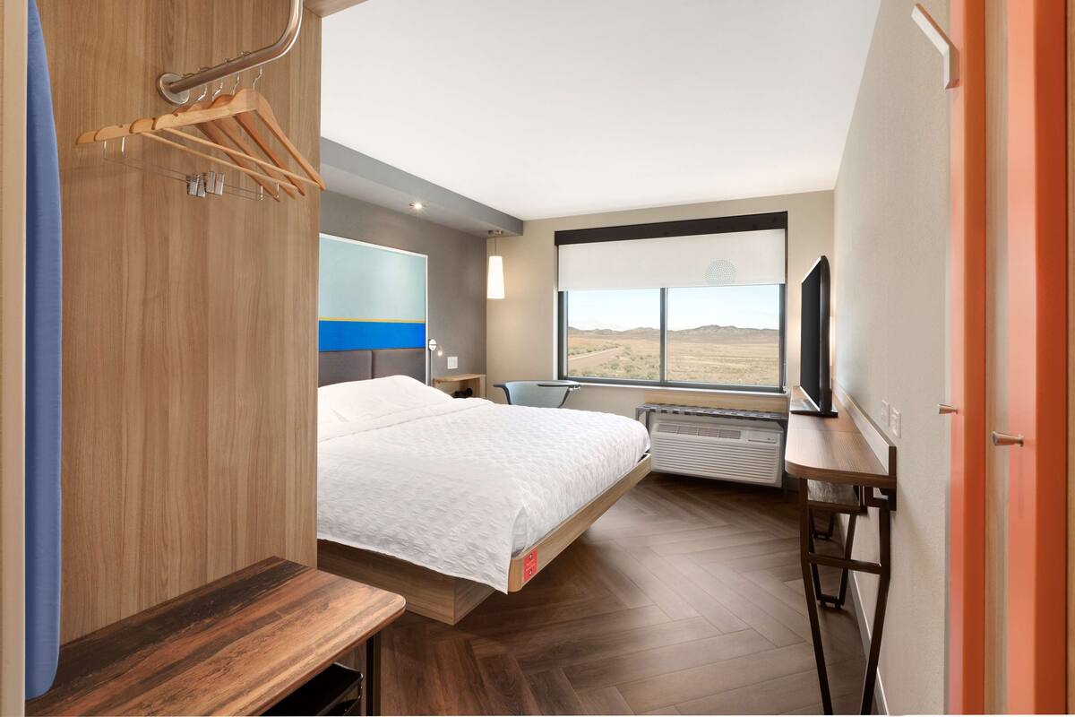 A modern hotel room with a bed, a desk, a TV, and a window with a desert view.
