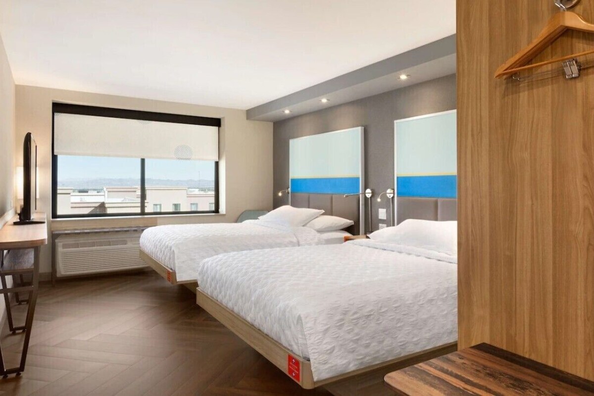 A hotel room with two beds, a desk, a large window, and a view of the cityscape.