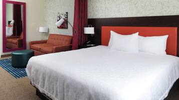 Habitación de hotel con una cama grande, cabecera roja, dos lámparas de noche, un espejo, cortina roja y pared con diseño.