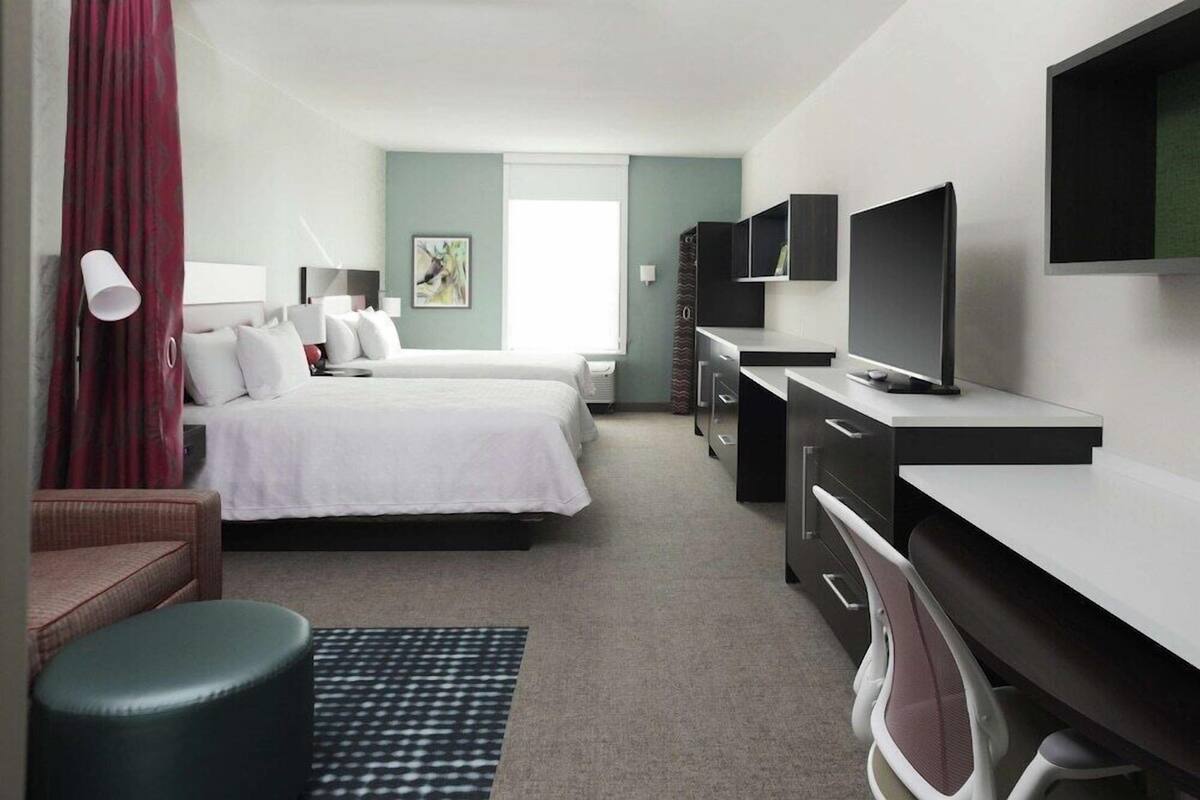 A hotel room with a large bed, a desk with a computer, a TV, and a window with curtains.