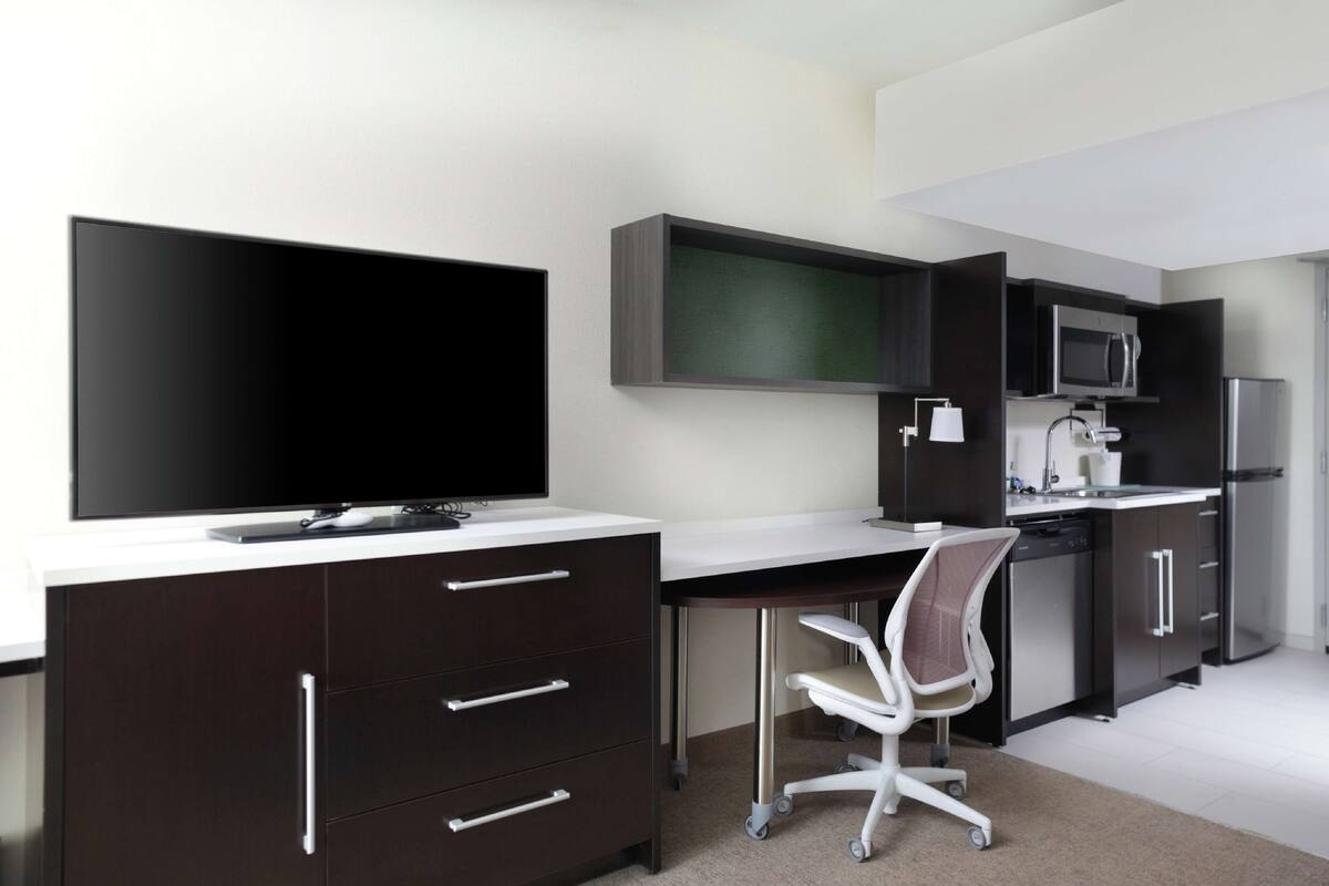 A modern kitchen with dark cabinetry, a flat-screen TV, a microwave, and a refrigerator.