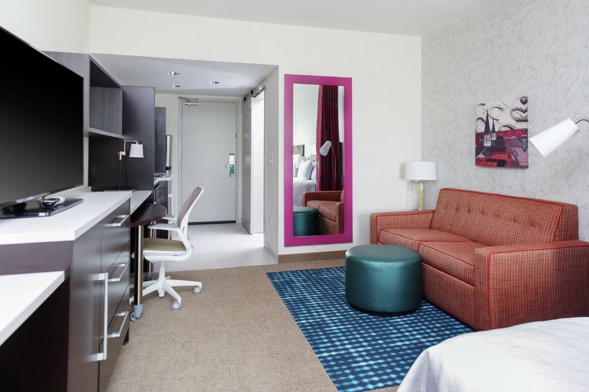 A modern hotel room with a desk, office chair, and a red sofa.