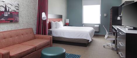 Una habitación de hotel con cama, sofá, escritorio y silla, televisor y ventana con cortinas.