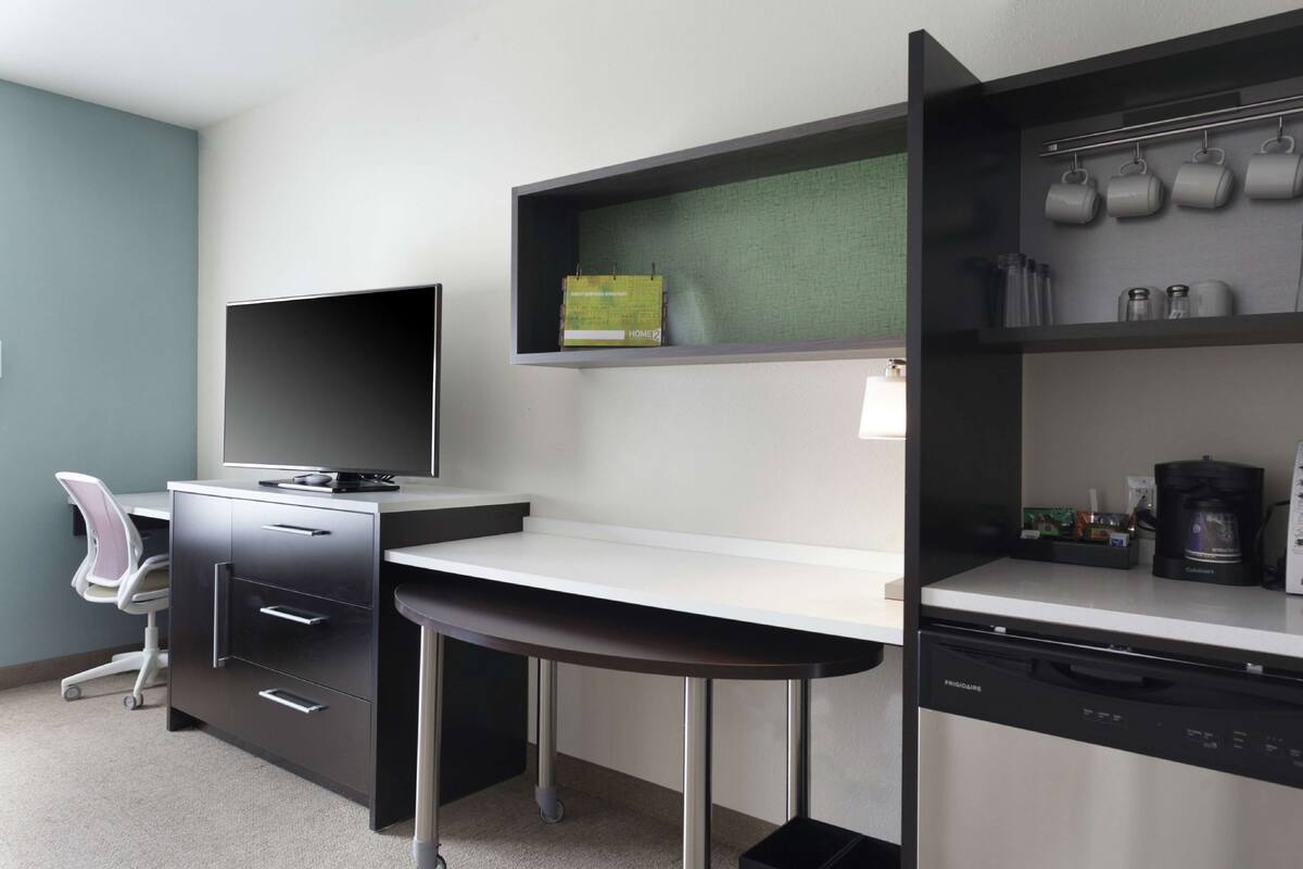 A modern kitchen with a built-in dishwasher, a coffee maker, and a shelf with kitchenware.