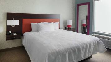 A hotel room with a large bed, a nightstand with a lamp, a mirror, and a window with a view.