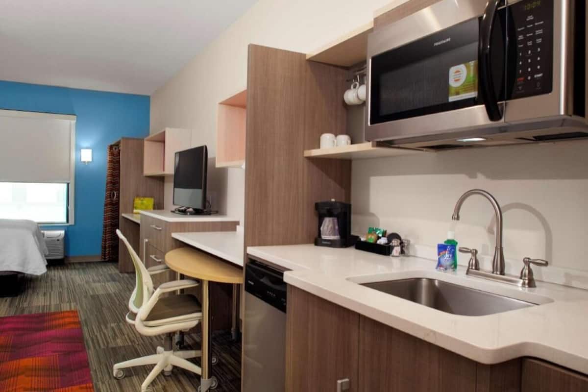 Een kleine hotelkamer met een kitchenette, een bed, een bureau en een stoel.