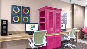 Un espace de bureau moderne avec un bureau en bois, deux chaises de bureau, une armoire rose et quatre œuvres d’art circulaires encadrées accrochées au mur.