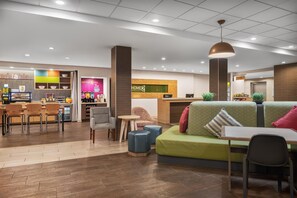 Een hotel lobby met een receptiebalie, een zithoek en een koffiebar.