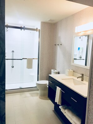 Une salle de bain moderne avec une douche à parois de verre, des toilettes blanches et un meuble-lavabo avec un miroir.