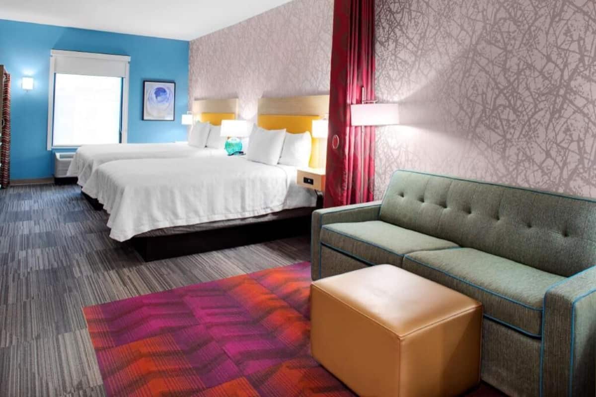 Een hotelkamer met twee bedden, een bank, een klein voetenbankje en een kamer met een patroon op de muur.