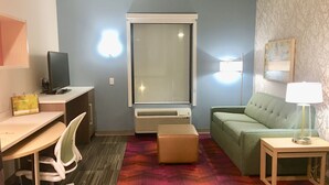 Une chambre d’hôtel équipée d’un bureau, d’une chaise, d’un canapé vert et d’une petite table avec une lampe.