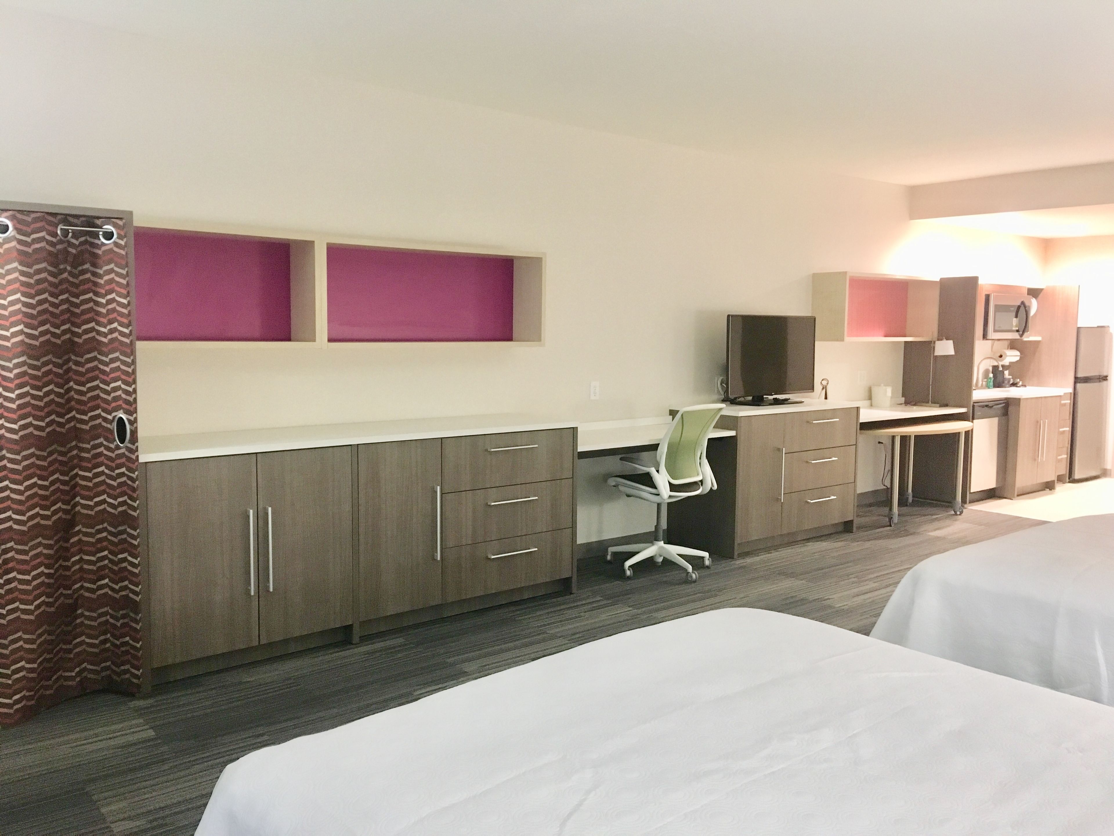 A hotel room with two beds, a desk with a chair, a television, and a microwave.