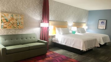 Una habitación de hotel con un sofá verde, una cama con ropa de cama blanca, un tapete estampado y un cuadro en la pared.