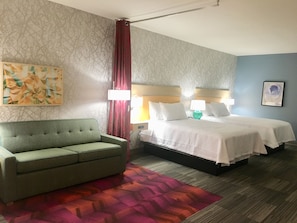 Ein Hotelzimmer mit einem grünen Sofa, einem Bett mit weißer Bettwäsche, einem gemusterten Teppich und einem Bild an der Wand.
