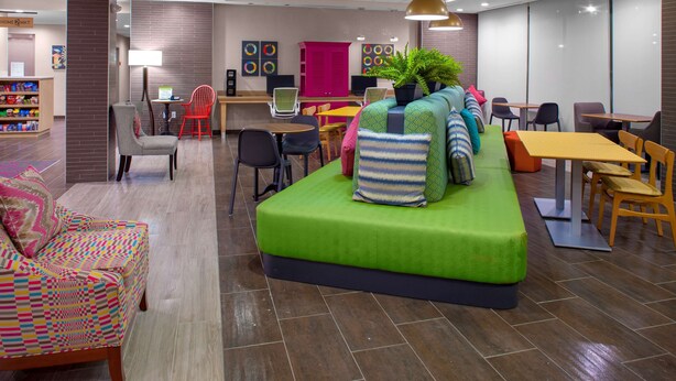 Un hall d’hôtel moderne avec un canapé vert, plusieurs espaces de détente, un comptoir d’accueil et un comptoir de restauration.