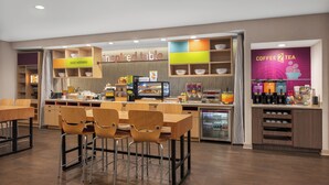 A modern cafe with wooden tables and chairs, a counter with a coffee and tea station, and a sign that reads "inspired table". - Home2 Suites by Hilton Lake Charles, LA (Lake Charles)