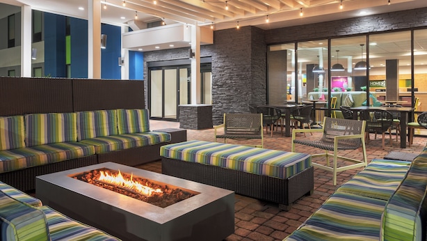 A modern outdoor seating area with a fire pit, cushioned sofas, and a dining area with tables and chairs. - Home2 Suites by Hilton Lake Charles, LA (Lake Charles)